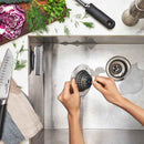 OXO sink strainer catching food debris in stainless steel drain with hands holding inverted basket
