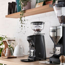 Mazzer Mini coffee grinder on wooden countertop with beans in hopper for home barista setup