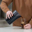Person pouring Toddy cold brew concentrate from dark gray chamber into glass with ice cubes
