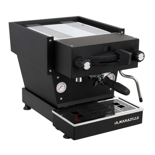 Person using La Marzocco Linea Mini espresso machine on wooden counter with stacked ceramic cups