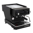 Person using La Marzocco Linea Mini espresso machine on wooden counter with stacked ceramic cups