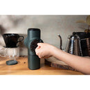 Person adjusting dark green Pietro Pro manual coffee grinder dial on wooden counter