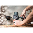 Hands operating dark green Pietro Pro manual coffee grinder crank on wooden surface