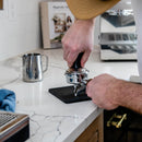 Barista tamping coffee grounds in wooden-handled portafilter for Ascaso espresso machine preparation