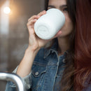 Woman drinking from white Fellow Carter Wide travel mug showing wide opening