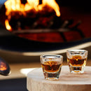 Two amber-filled cortado glasses near warm firelight background
