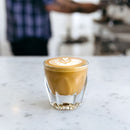 Faceted cortado glass with latte art rosetta on white marble