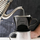 Pouring water into Kalita 102 black ceramic dripper on glass mug